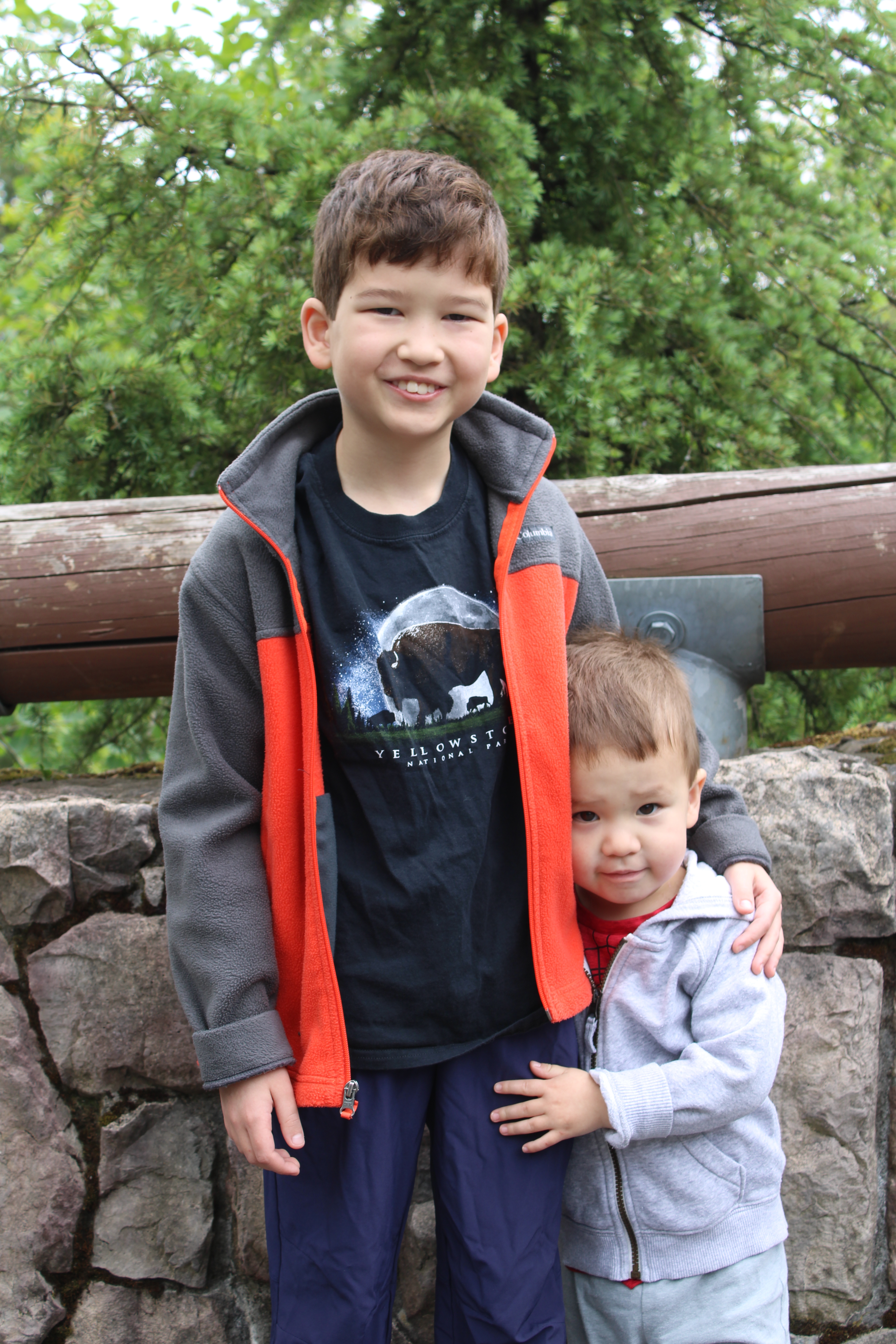 Two young boys smile and stand in front of a stone wall.