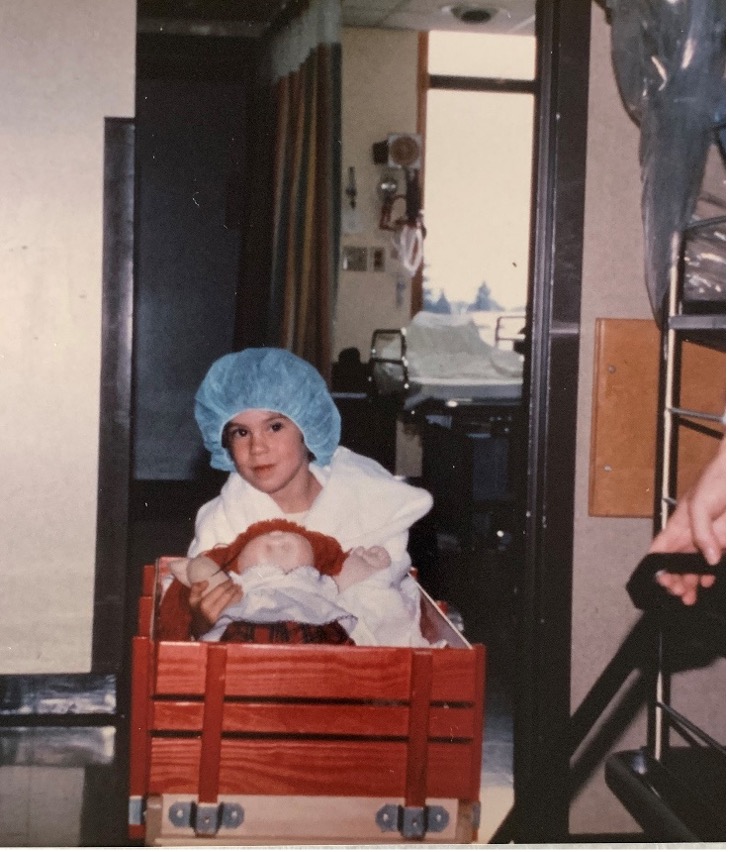 Picture1 Sarah Horn as a child holds a Cabbage Patch doll in a red wagon being pulled.