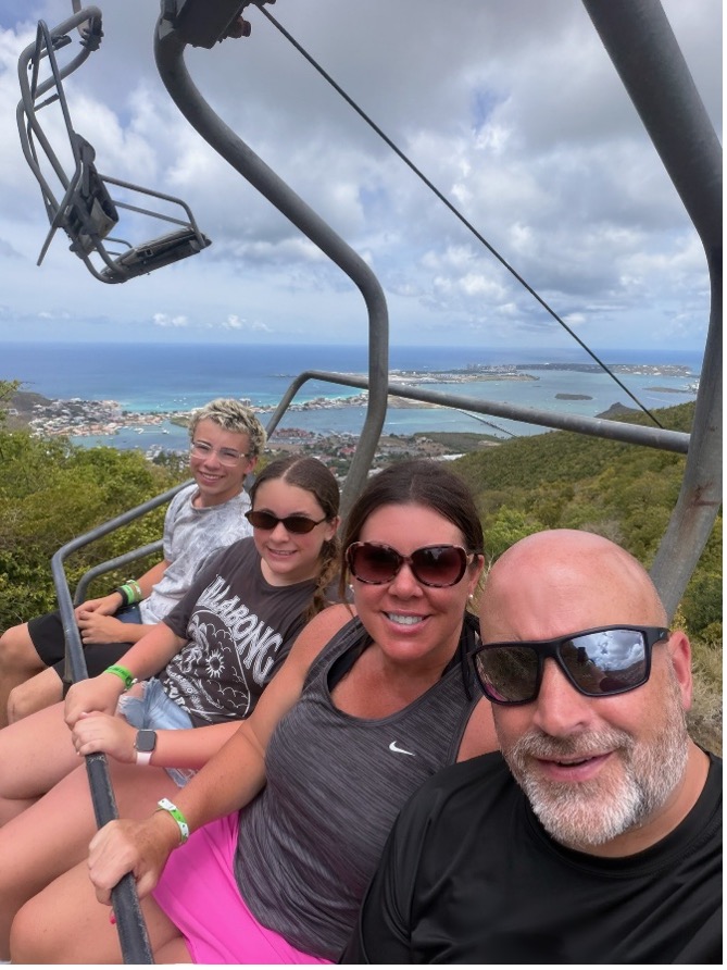 Picture7 Sarah Horn with her husband and two children on a ski lift with green hills and water behind.