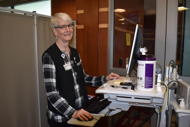 Women is standing next to a computer monitor smiling at the camera.