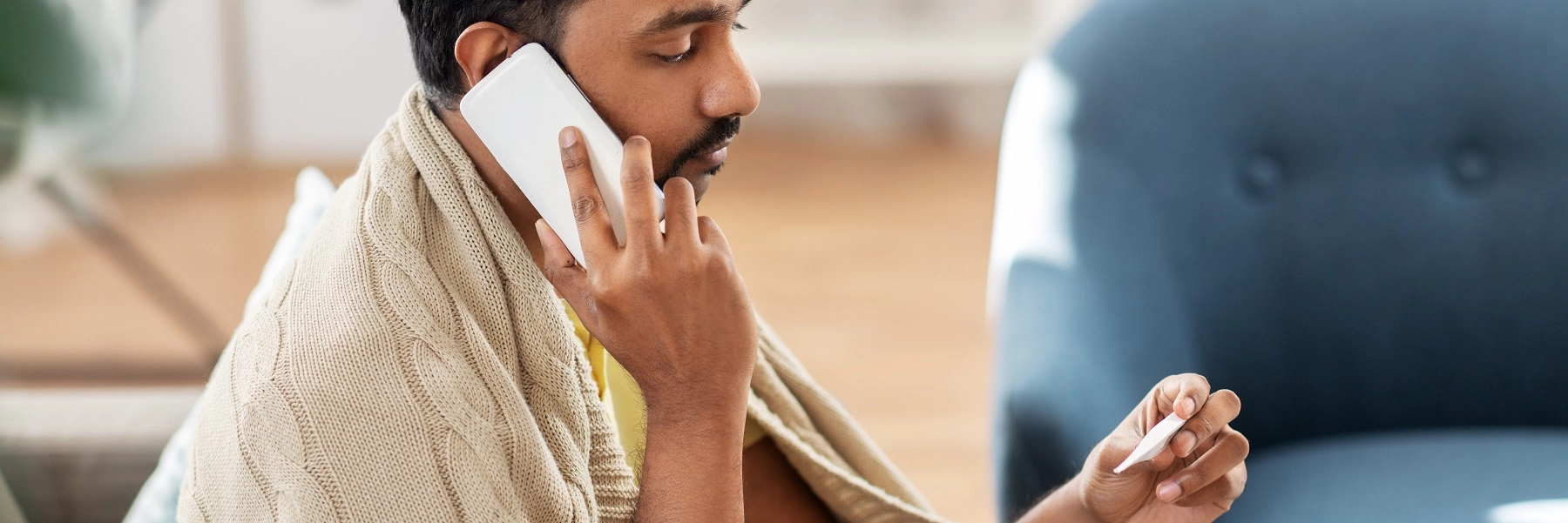 Darker-skinned man with mustache looks at thermometer while making a phone call.