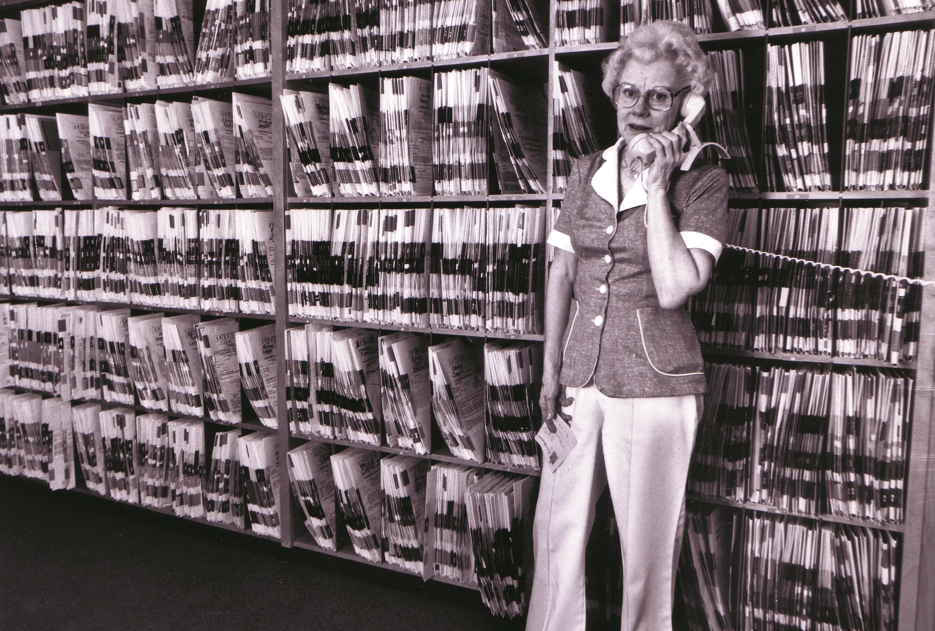 A nurse stands in front of a wall of medical records, 1982.