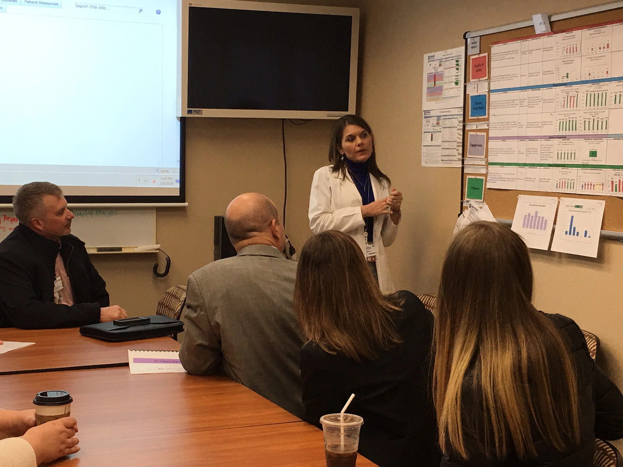 A woman in a conference room with others looking at charts on a bulletin board.