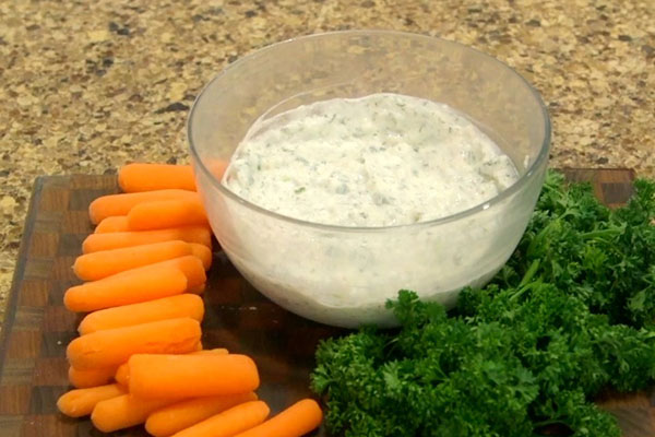 Glass bowl filled with healthy ranch dip with mini carrots on the side.