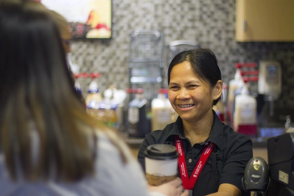 Barista hands beverage to employee.