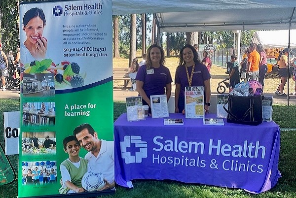 Two Salem Health CHEC staffers standing behind an information table at a recent community event.