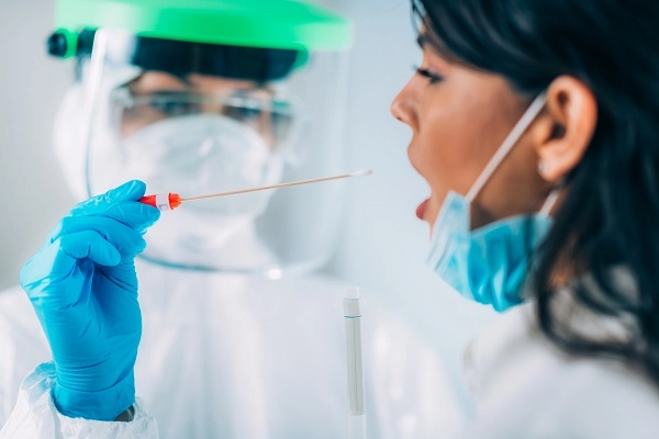 A medical worker wearing a protective face shield prepares to test a patient for coronavirus.