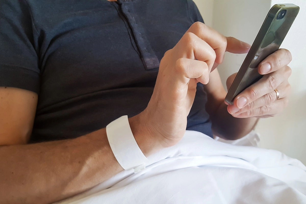A male patient uses a smartphone in a hospital bed.