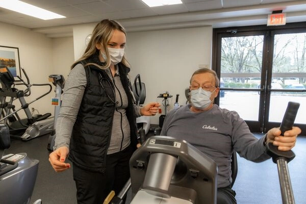 Cardiac rehab therapist assiting patient on an exercise bike