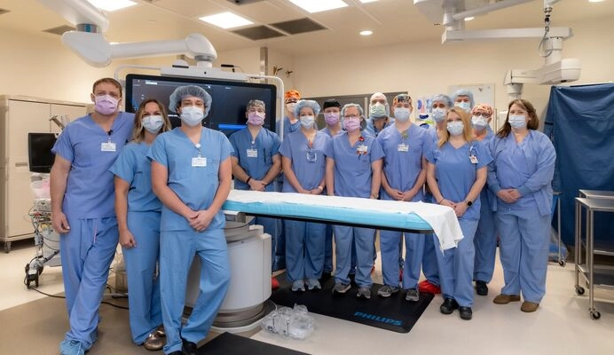 Cath lab team standing in the cath lab all wearing scrubs