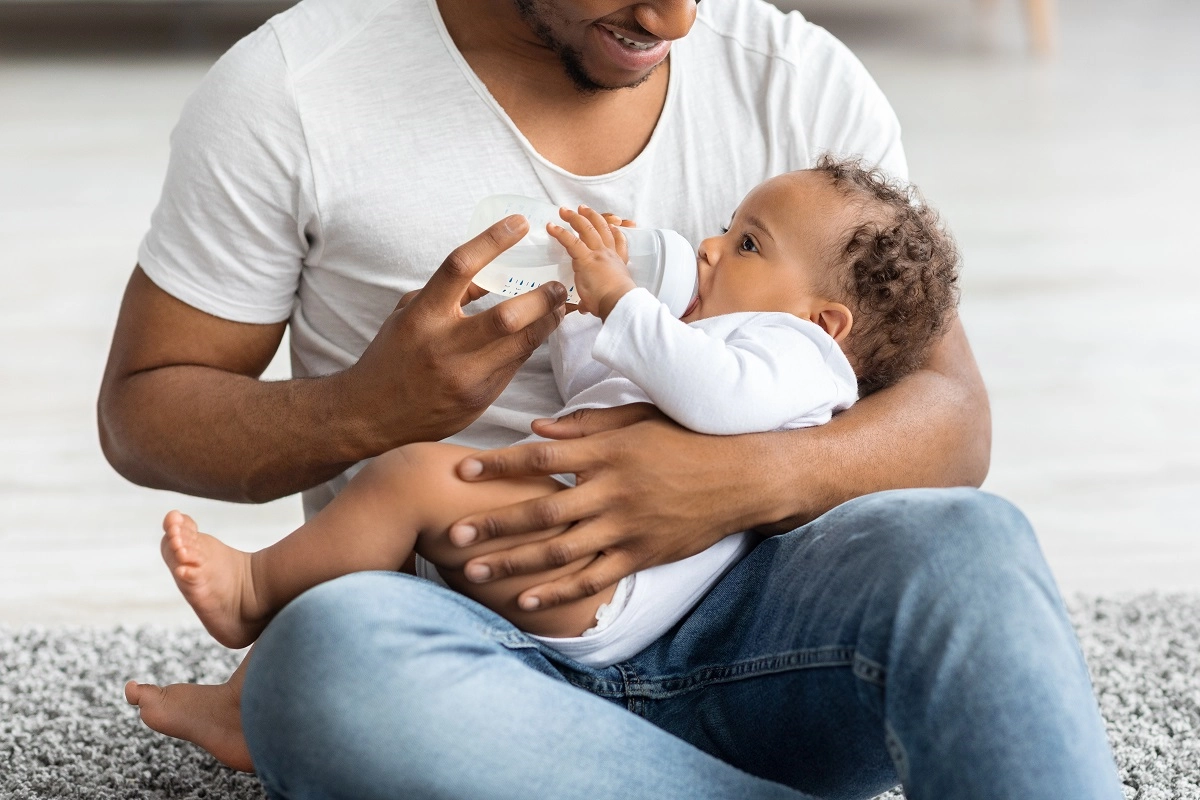 A dad bottle feeding his curly-haired baby.