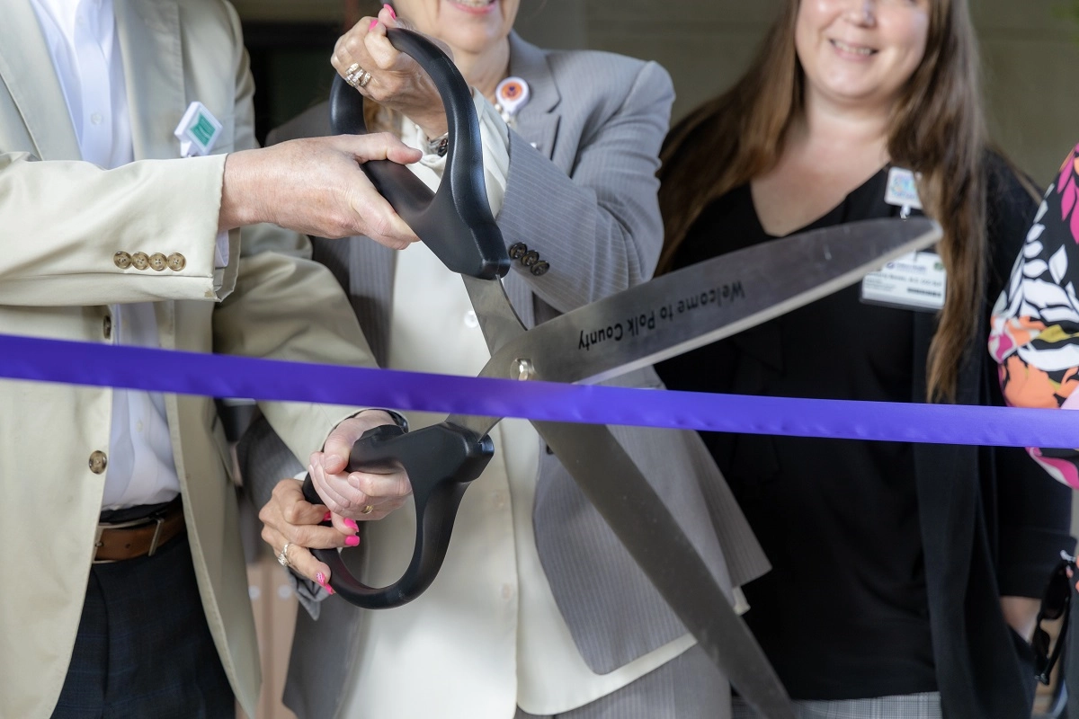 Three sets of hands on a giant pair of novelty scissors cutting a ribbon