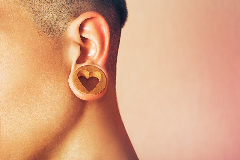 Close up of a gauged ear with a large wooden plug with a heart on it