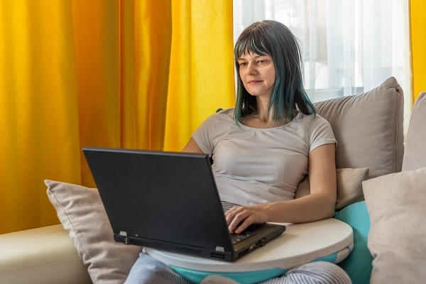 A woman in pajamas using a laptop on the couch.