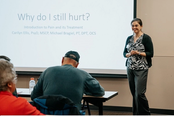 Instructor teaching Pain 101 class in front of a screen that says "Why do I still hurt?"