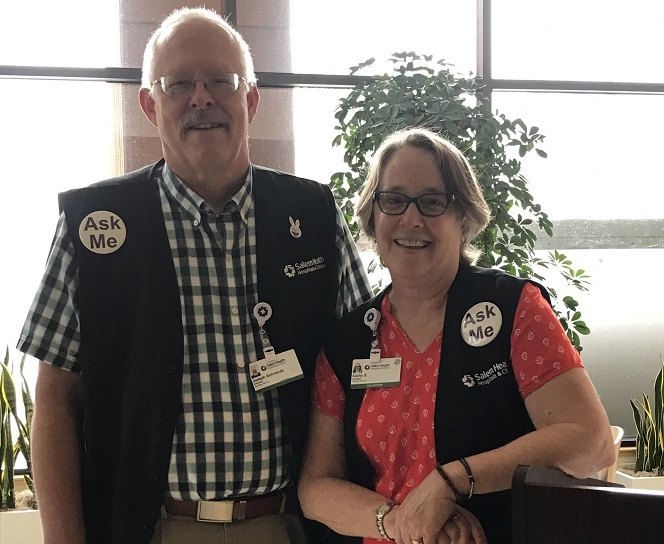 Male and female volunteer greeters in black vests smile at the camera.