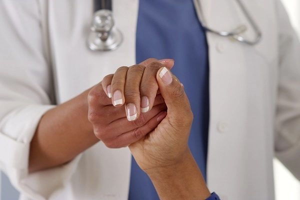 A doctor in a white coat holds the hand of a patient