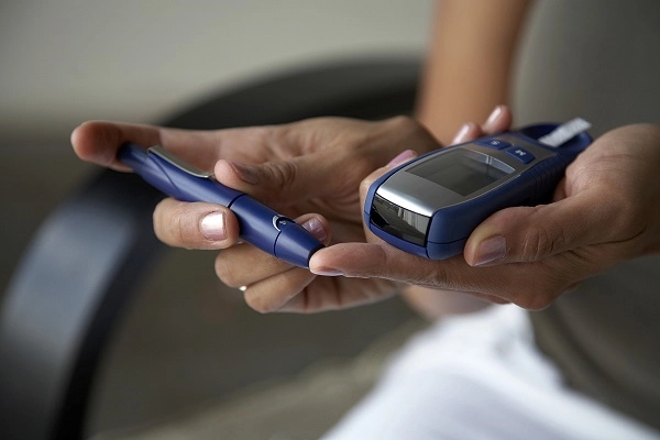 A hand using a device to prick a finger to draw blood for a glucose test.