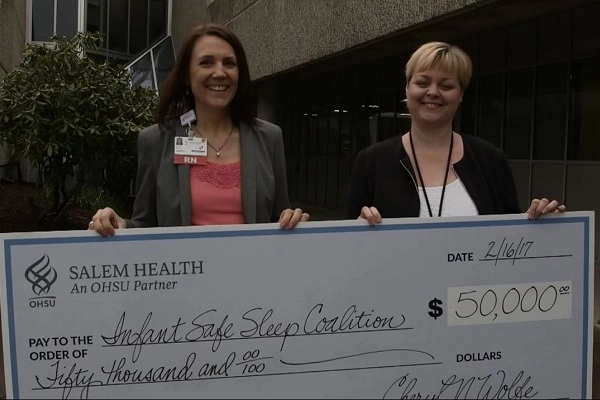 Two women hold a giant check made out to Infant Safe Sleep Coalition